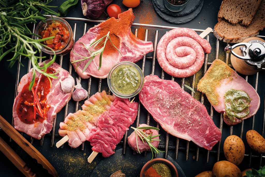 Auswahl an frischem Grillfleisch mit teaks, Koteletts, Bratwurst und Fleischspießen, angerichtet mit Kräutern, Gewürzen und Grillsaucen.